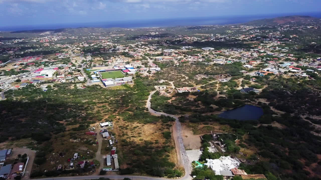 vista aérea de un lago natural y una cancha de tenis en el centro de aruba con el mar caribe al fondo