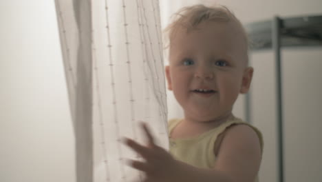 Playful-baby-girl-having-fun-with-curtain-at-home