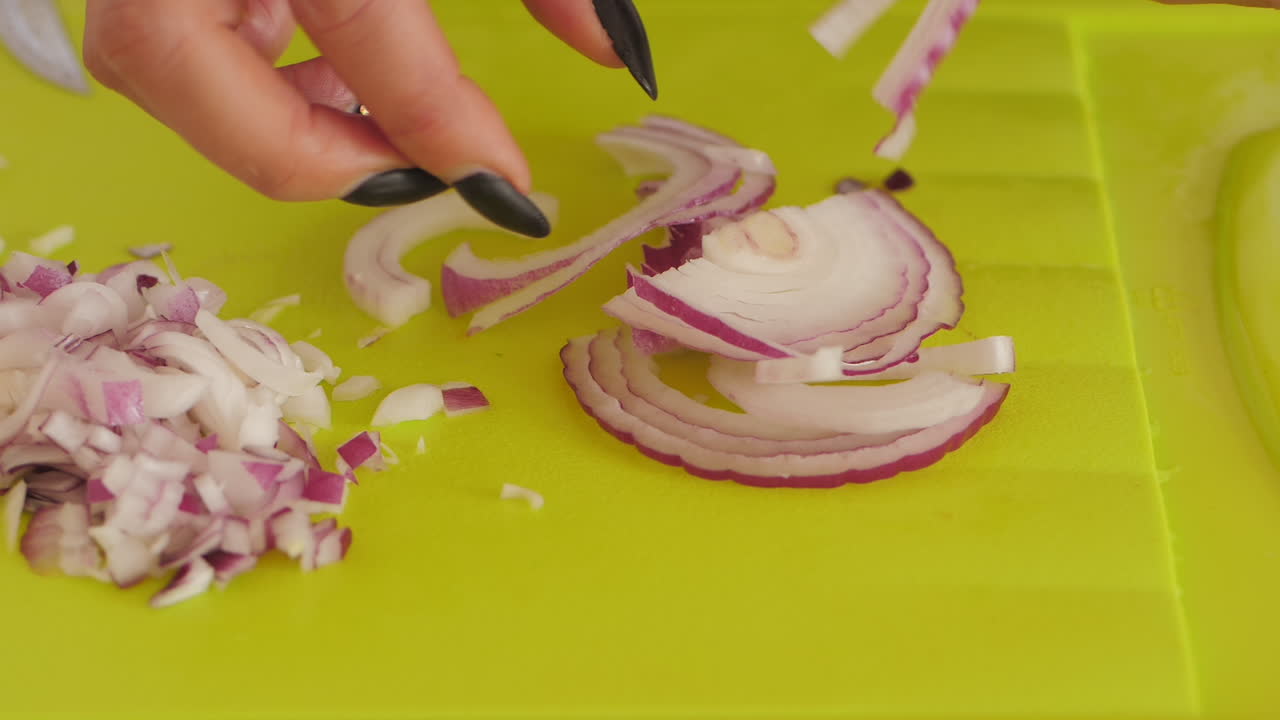 Women separating rings from red onion on chopping board