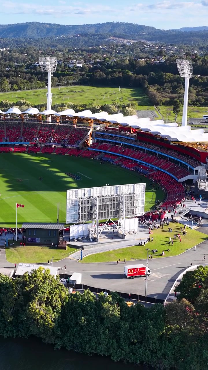 High angle drone shot of a sunny sports stadium with floodlights and green field.