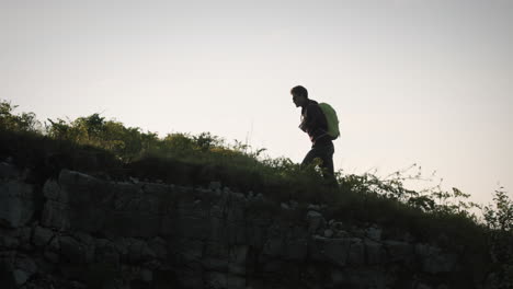 Man-walking-uphill-with-a-bright-green-backpack-and-sunglasses