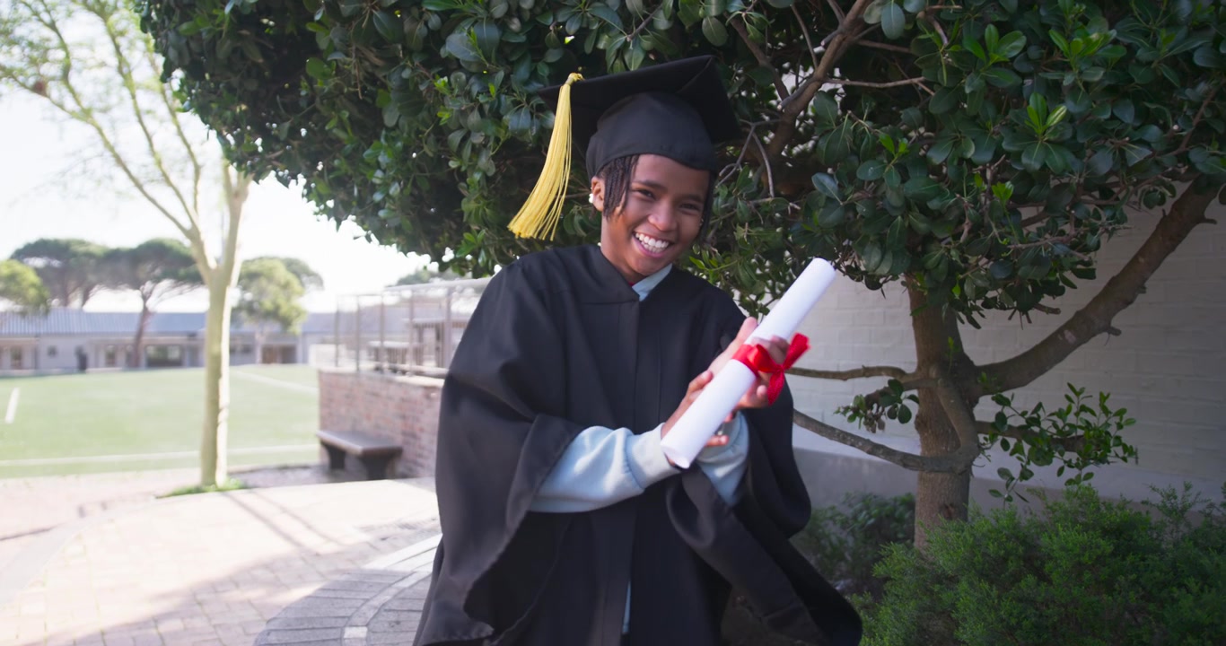 Pria muda Afrika mengenakan toga merayakan, memegang diploma dan tertawa, menarik jumbai di sekolah