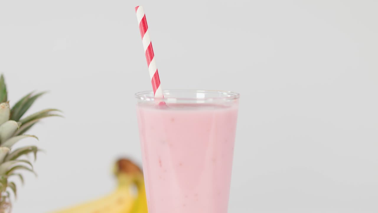 Una mano decora un cremoso frullato rosa con una fragola fresca in un bicchiere, illuminazione brillante da studio, scatto statico