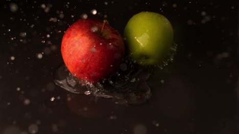 green and red apples falling on wet black surface