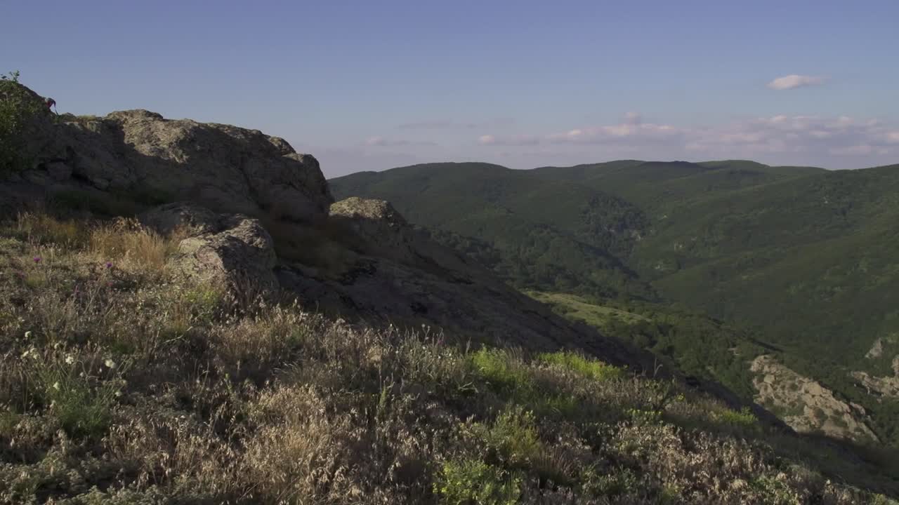 Rocky ledge at a mountain viewpoint. The view includes a vast green valley and distant hills. Daytime with clear skies and bright sunlight. Stara planina nearby Sliven town. Balkan Mountains