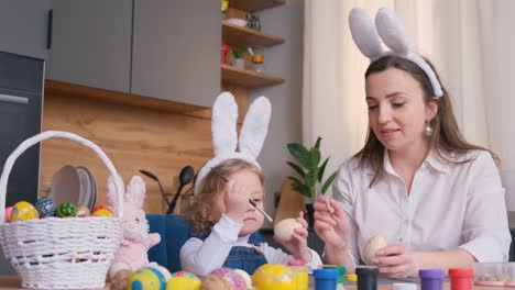 mother and daughter painting easter eggs together at home. bright festive decorations, joyful atmosphere, creativity, and bonding. colorful paints, bunny ears, and spring mood