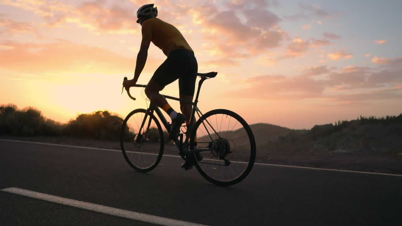 The athlete on a bike is seen in slow motion conquering a mountain serpentine, cherishing the island's view, epitomizing a devotion to a healthy lifestyle at sunset