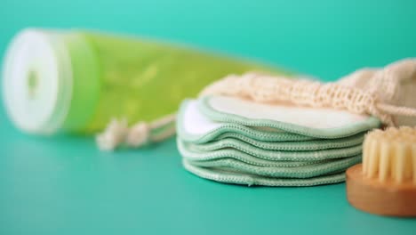 eco-friendly personal care products: reusable pads, brush, and bottle on a green background