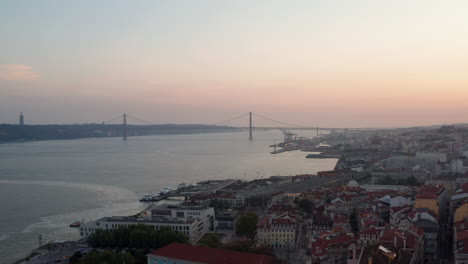 Aerial-slider-view-of-Ponte-25-de-Abril-red-bridge-across-the-sea-canal-in-Lisbon,-Portugal-with-houses-in-old-city-center