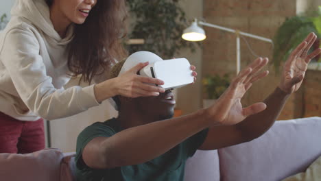 hombre negro alegre usando gafas vr con la ayuda de su esposa en casa