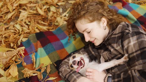 curly woman lying on a plaid with her jack russell terrier puppy in autumn park, top view