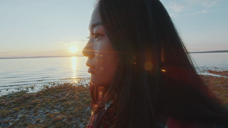 contemplative woman looking at scenic lakeshore during golden hour sunset