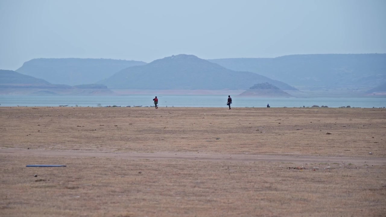 indian people are walking near backwater of nagarjuna sagar, sand with water and hill mountain at vizag colony, azmapur, nalgonda, telangana, india. day time, stable shot, 4k.