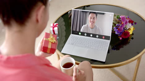 caucasian woman holding red gift using laptop with caucasian man on screen