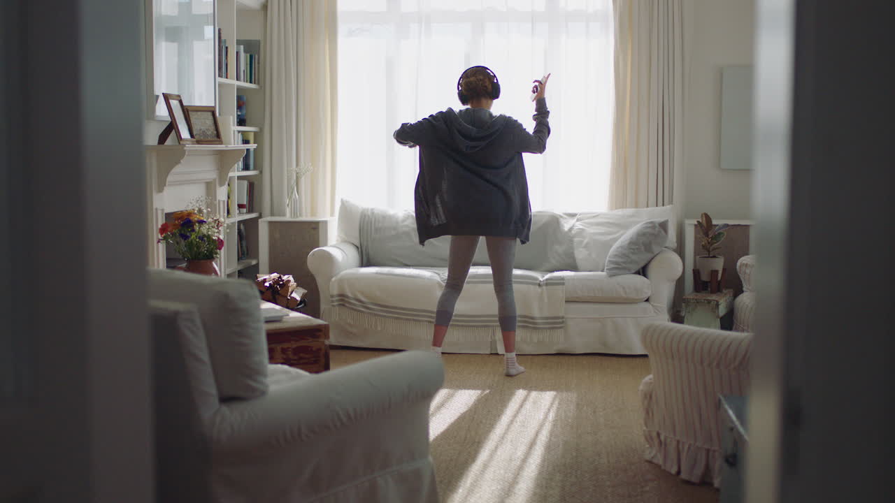 행복한 젊은 여성이 집에서 춤을 추고 즐겁게 음악을 듣고 헤드폰을 착용하고  ⁇ 키 댄스 동작으로 주말 축제를 즐기고 있습니다.