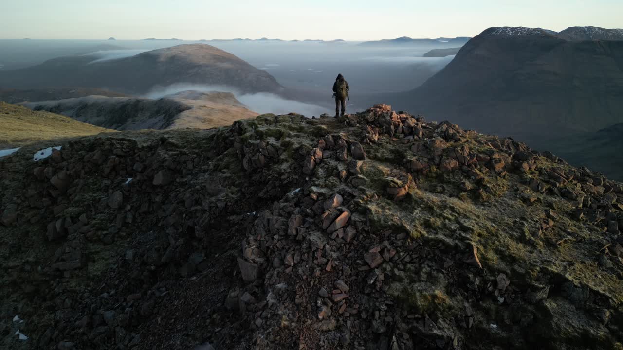 Glen Coe, Scottish Highlands - aerial over the mountains in winter with hill walker standing on summit of mountain - reveal of glen and Rannoch Moor