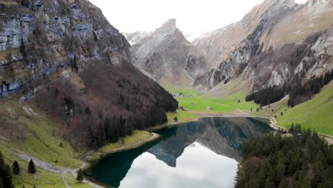 Aerial-flyover-over-Seealpsee-in-Appenzell,-Switzerland-with-a-reflection-of-the-Alpstein-peaks-on-the-lake