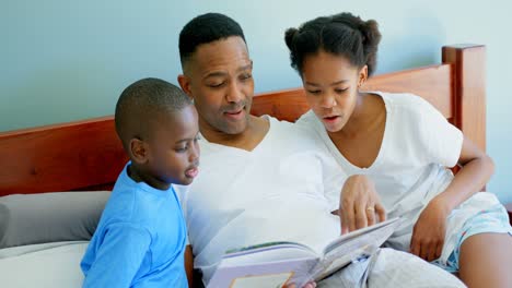 front view of mid adult black father with his children reading story book in bedroom of comfortable