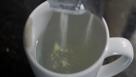 Close-up-shot-over-orange-juice-powder-been-poured-into-water-in-a-cup-before-mixing-it-with-black-background