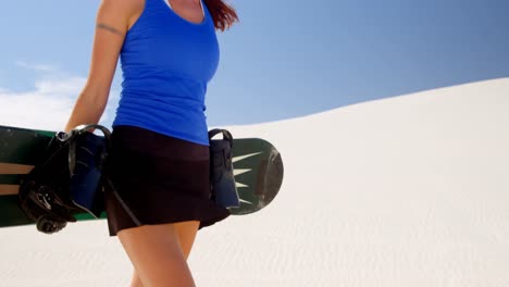 mujer caminando con tabla de arena en el desierto 4k