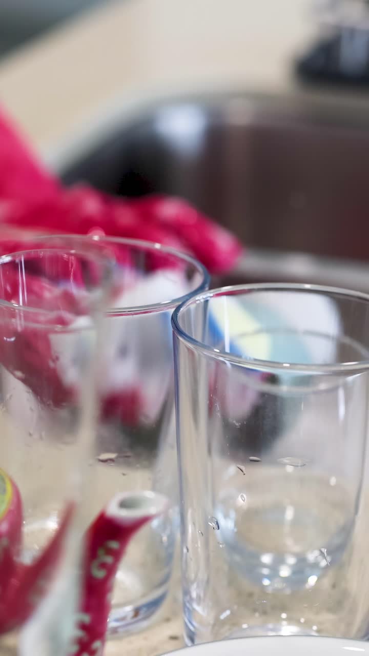 Una persona che indossa guanti rosa lava i bicchieri in un lavello da cucina con acqua saponata.