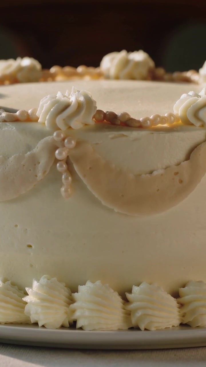 Vertical video: Panning low angle shot moving upward over table, showing cake with rosettes, pearls