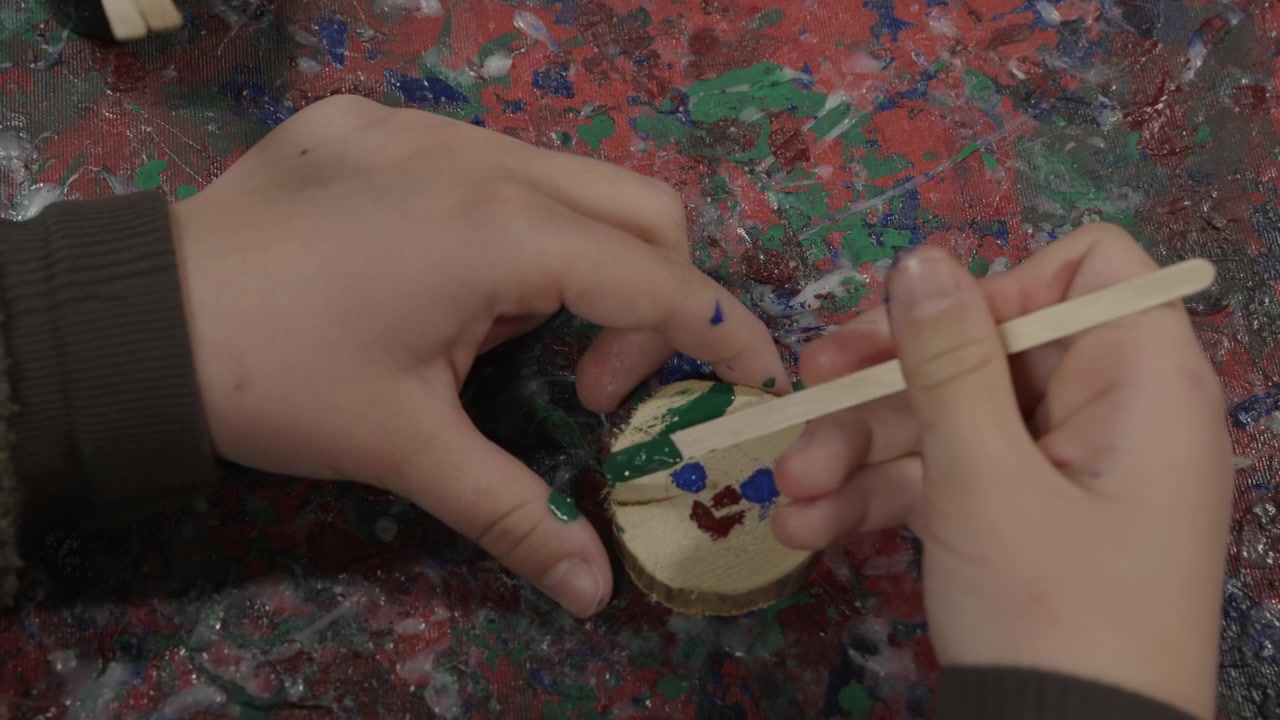 Child Painting a Small Wooden Disc with Green Paint