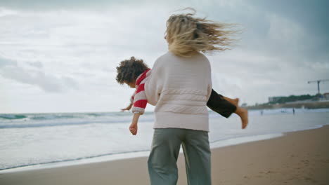 Fröhliche-Mutter-Dreht-Ihr-Kind-Am-Herbststrand.-Lächelnde-Babysitterin-Spielt-Flugzeug