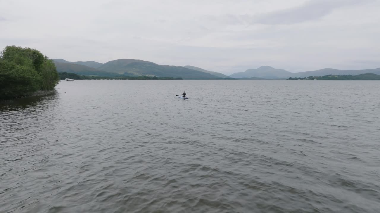loch lomond 해안에서 패들보드를 타는 젊은 여성의 느린 추적 샷