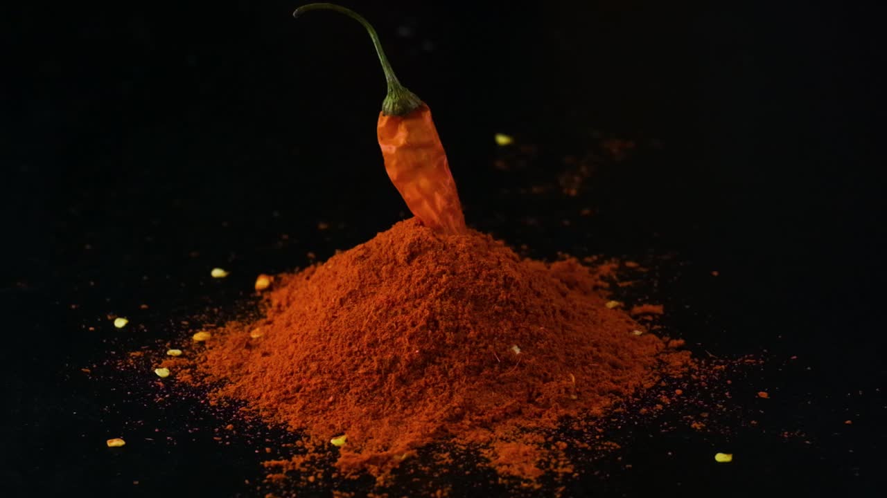 Peperoncino rosso in polvere e fiocchi di peperoncino rosso con semi sulla superficie del tavolo con sfondo nero.