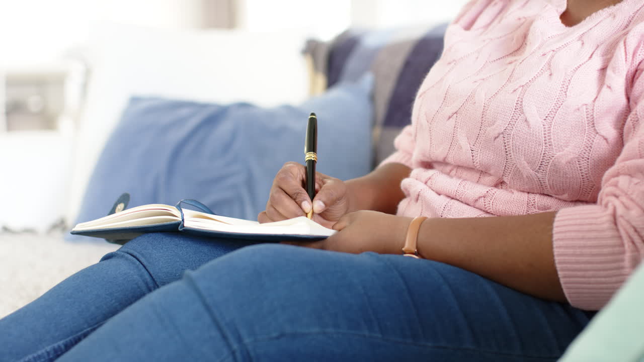 African American woman writes in a notebook while seated on a couch at home