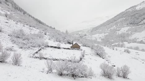 Toma-Aérea-De-Una-Solitaria-Casa-Rústica-Nevada-En-Medio-De-Las-Montañas-De-Un-Valle-En-Los-Pirineos-Españoles-En-Un-Día-Nublado