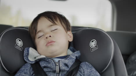 trip with a child - a multi-ethnic two-year-old boy naps in a car seat in the back seat of a car