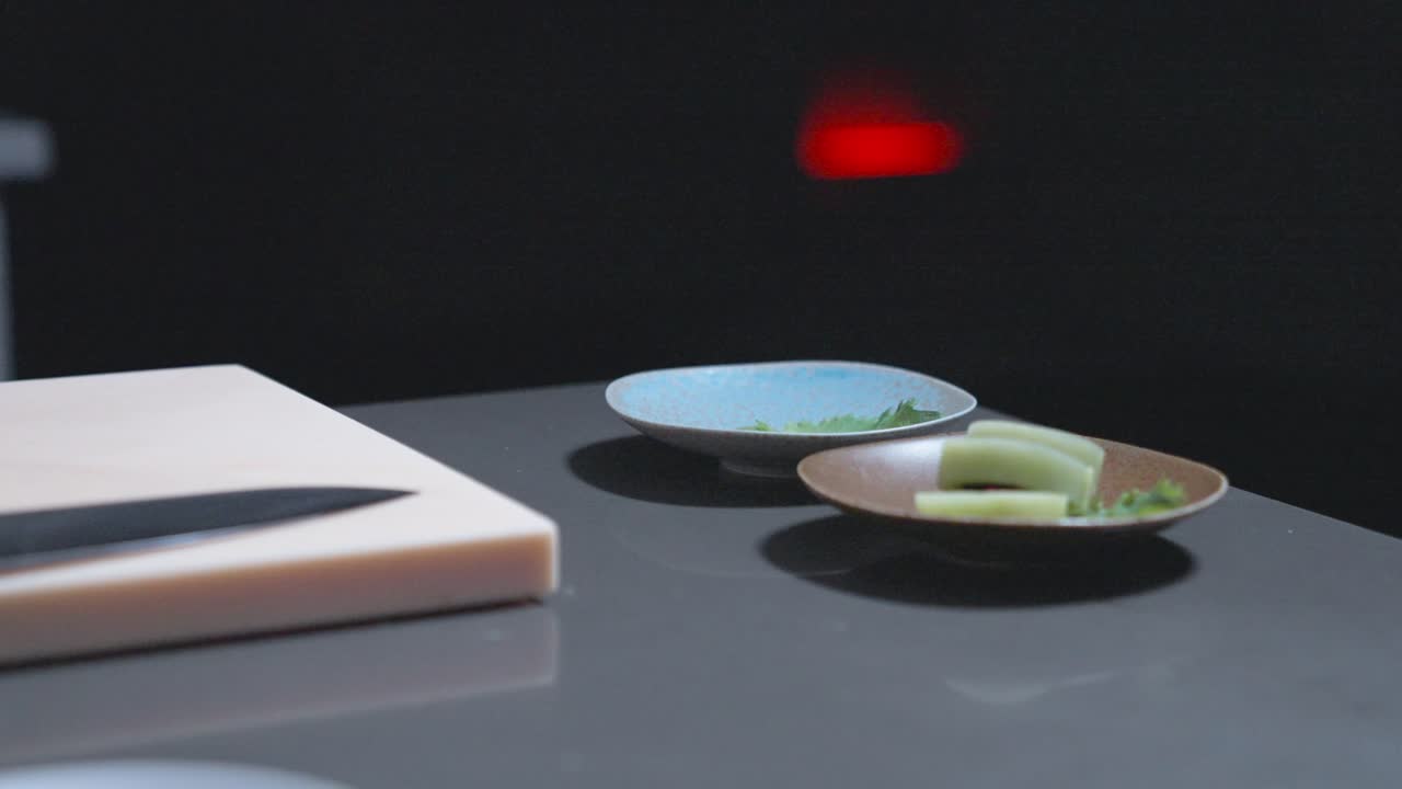A chef carefully places cucumber sushi rolls into a bowl, showcasing precise sushi preparation. Ideal for highlighting fresh sushi, Japanese cuisine, and culinary techniques in food presentations.