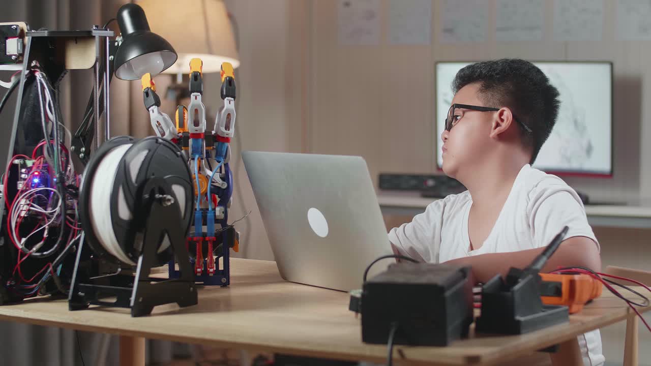 귀여운 아시아 소년은 집에서 노트북에서 사이보그 손에 대해 일하고 있습니다.