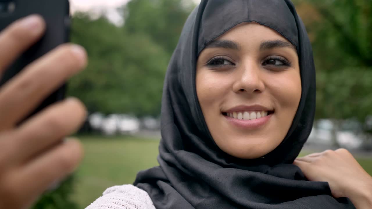 Young happy muslim womanin hijab is making selfie on smartphone in blue weather, communication concept, religious concept