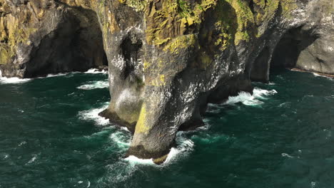 Aerial-view-of-birds-flying-around-the-Elephant-rock,-in-sunny-Heimaey,-Iceland