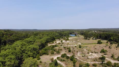 Flying-over-undeveloped-land-towards-river,-work-truck-below-driving-on-back-roads---Aerial-footage-of-the-Blanco-river-in-Wimberly,-TX