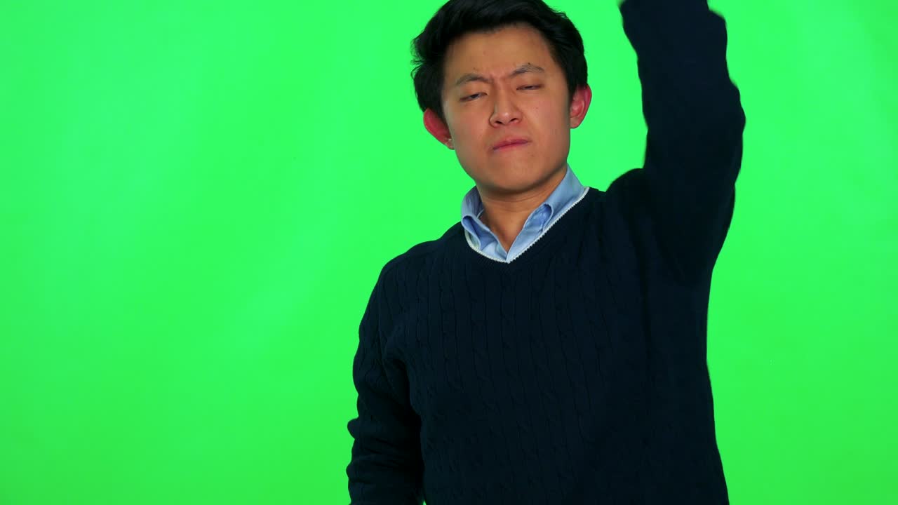 젊은 아시아 남자가 화를 내며 카메라를 향해 주먹을 흔들고 있습니다. - 그린 스크린 스튜디오