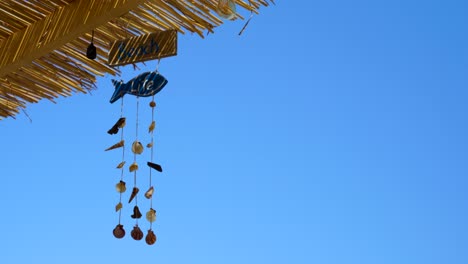 decorations with sea shells hanging on straw roof of beach bar with blue sky copy space