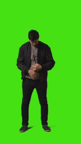 video vertical de larga duración de un joven que responde una llamada en un teléfono móvil de pie contra la pantalla verde 2