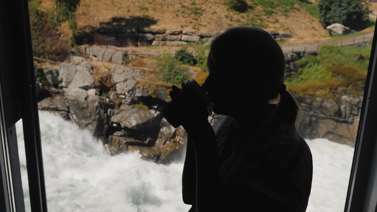 silueta de una mujer bebiendo una bebida caliente en un café junto a la ventana en las montañas de fondo y un