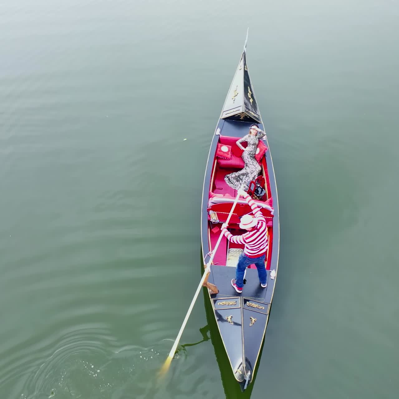 Beautiful woman sailing in gondola. Gondolier with oar moving boat slowly. Gondola floating the calm river in the evening.