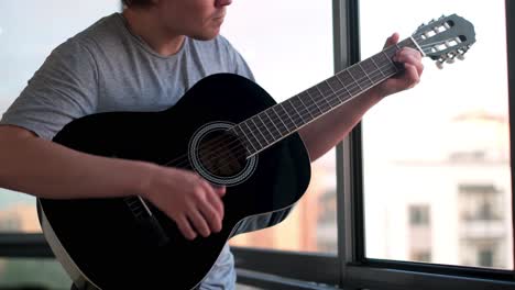 man playing acoustic guitar at a window