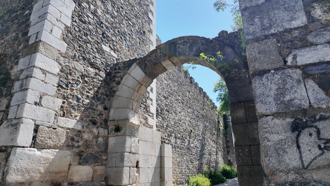 Ancient stone archway in the Castle of Beja, Portugal, with clear skies and greenery