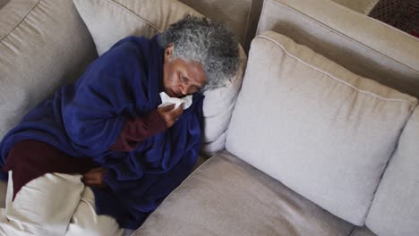 Sick-senior-african-american-woman-covered-with-blanket-sneezing-while-lying-on-the-couch-at-home