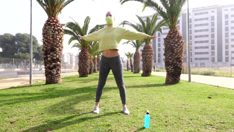 woman-with-mask-exercising-on-grass-in-avenue-surrounded-by-palm-trees