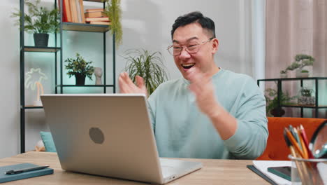 Amazed asian man use laptop computer receive good news message shocked by victory celebrate win