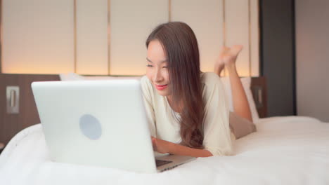 close up woman lying prone on a bed works on her laptop