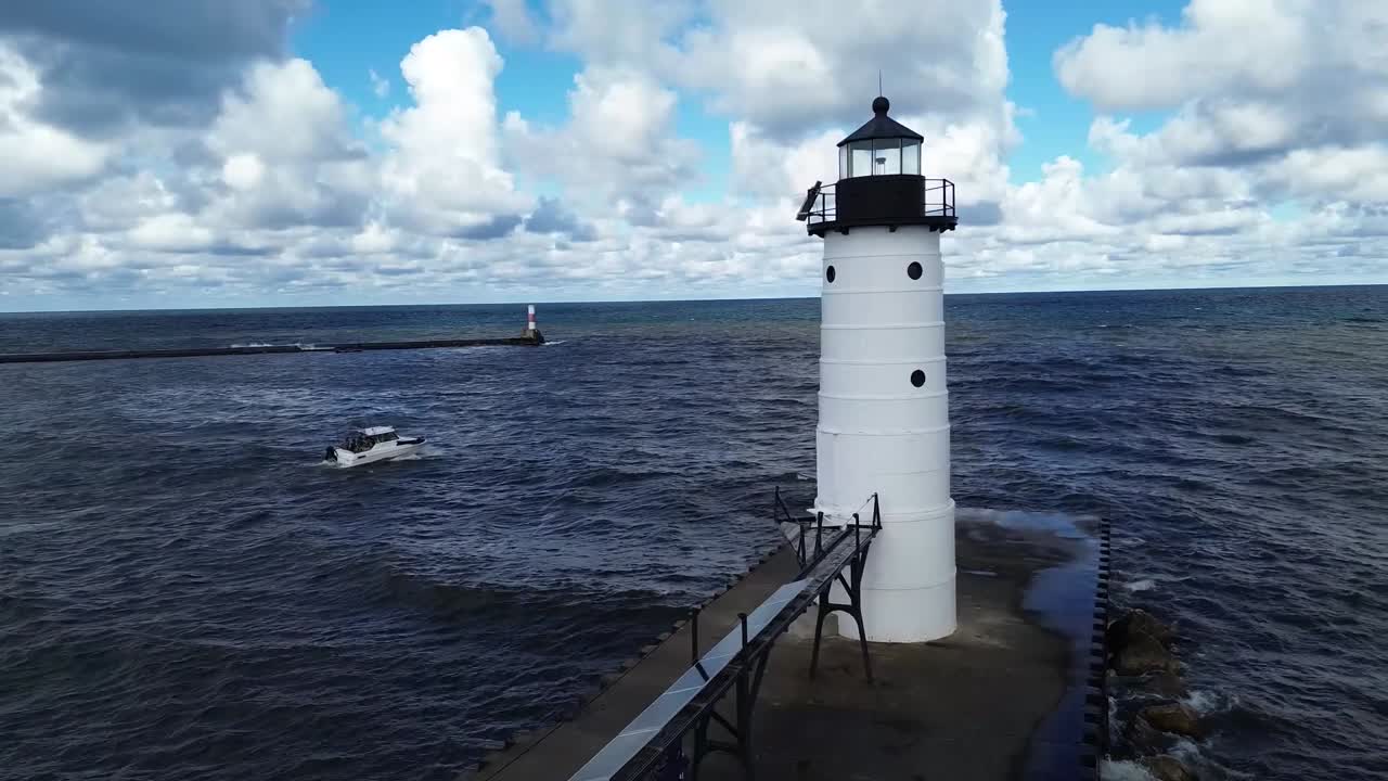 White lighthouse stands at end of long pier surrounded by choppy water, dramatic clouds and blue sky, wide seascape atmosphere, boat sailing nearby in dynamic coastal scene